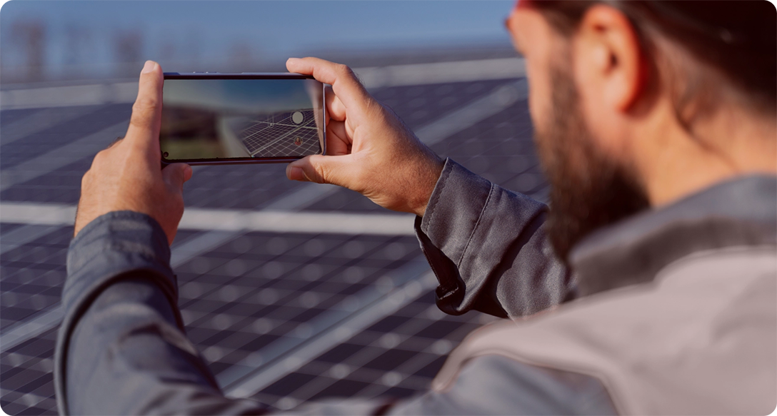 Roofer taking a picture of a solar panel covered roof with the smartphone camera in landscape mode.