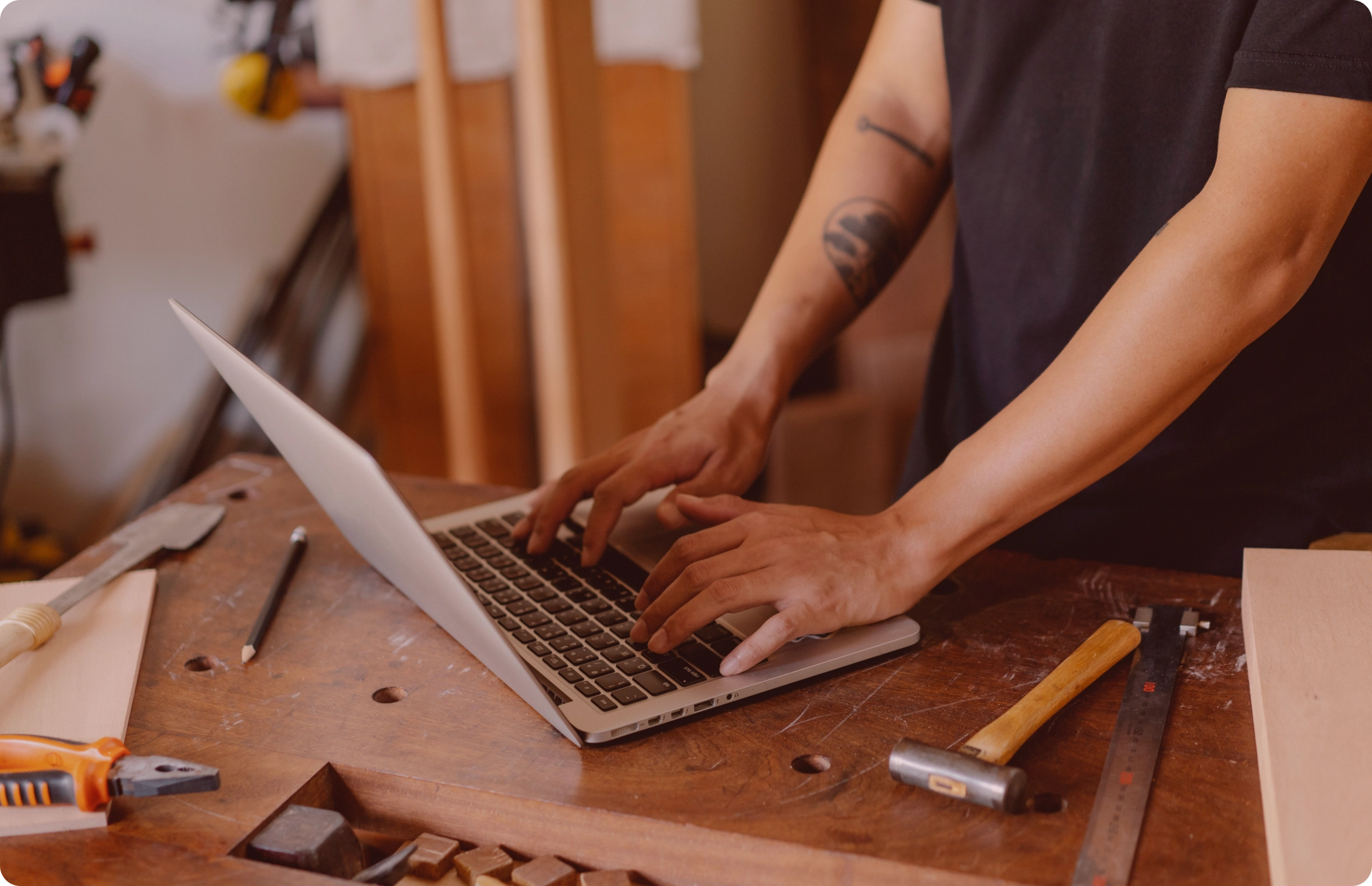 Man operating a laptop on a workbench. Tools laying next to it.